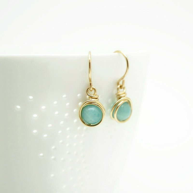 14k gold filled oorbellen met Amazoniet, hangend aan een witte waxinelichthouder met subtiele structuur.