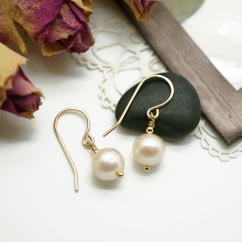 Detailweergave van 14k gold filled oorbellen met een glanzende witte zoetwaterparel, verfijnde afwerking zichtbaar.