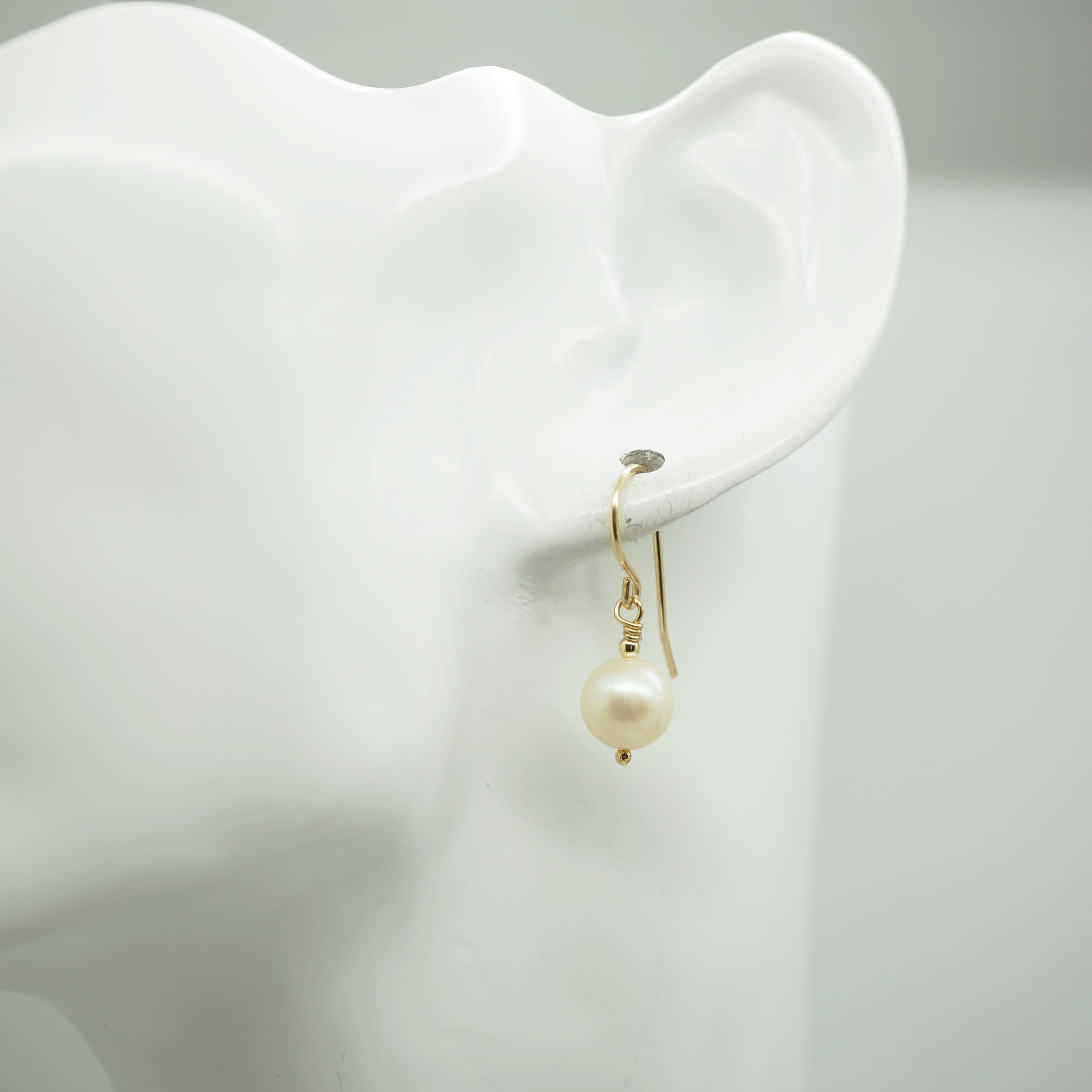 Klassieke gold filled oorbel met witte zoetwaterparel gedragen aan oor, elegante uitstraling in beeld.