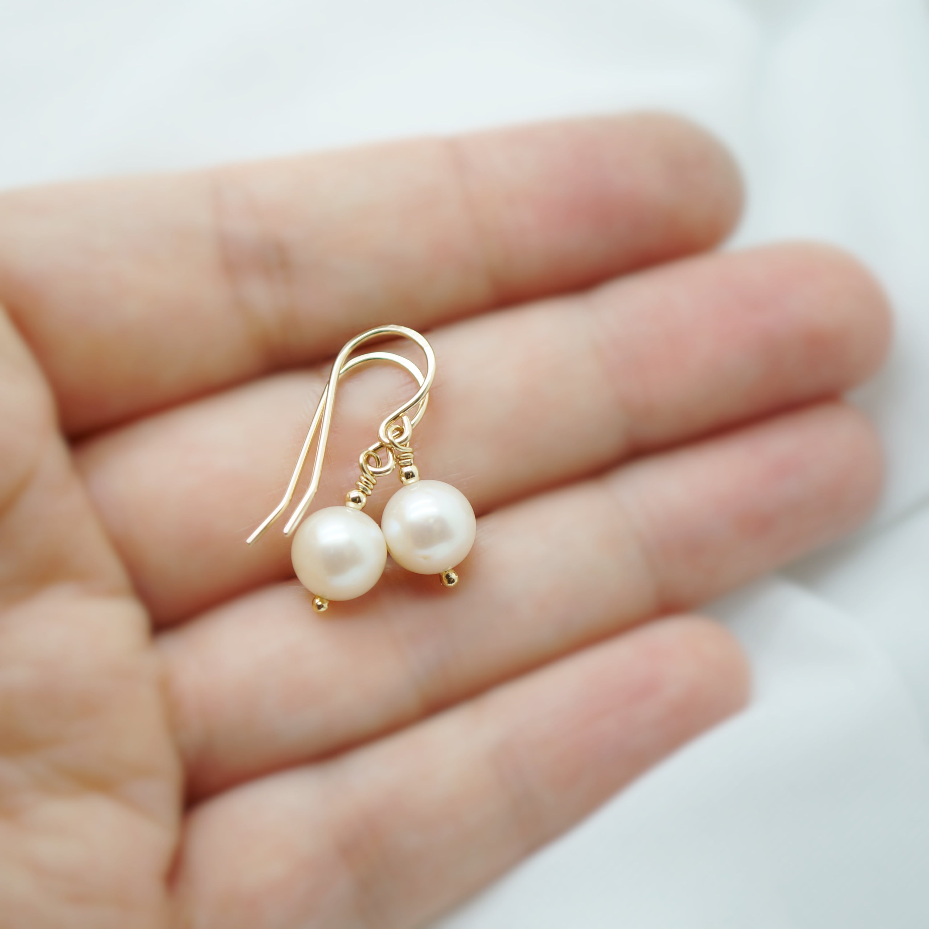 14k gold filled oorbellen met witte zoetwaterparel op hand getoond voor schaal en detail.