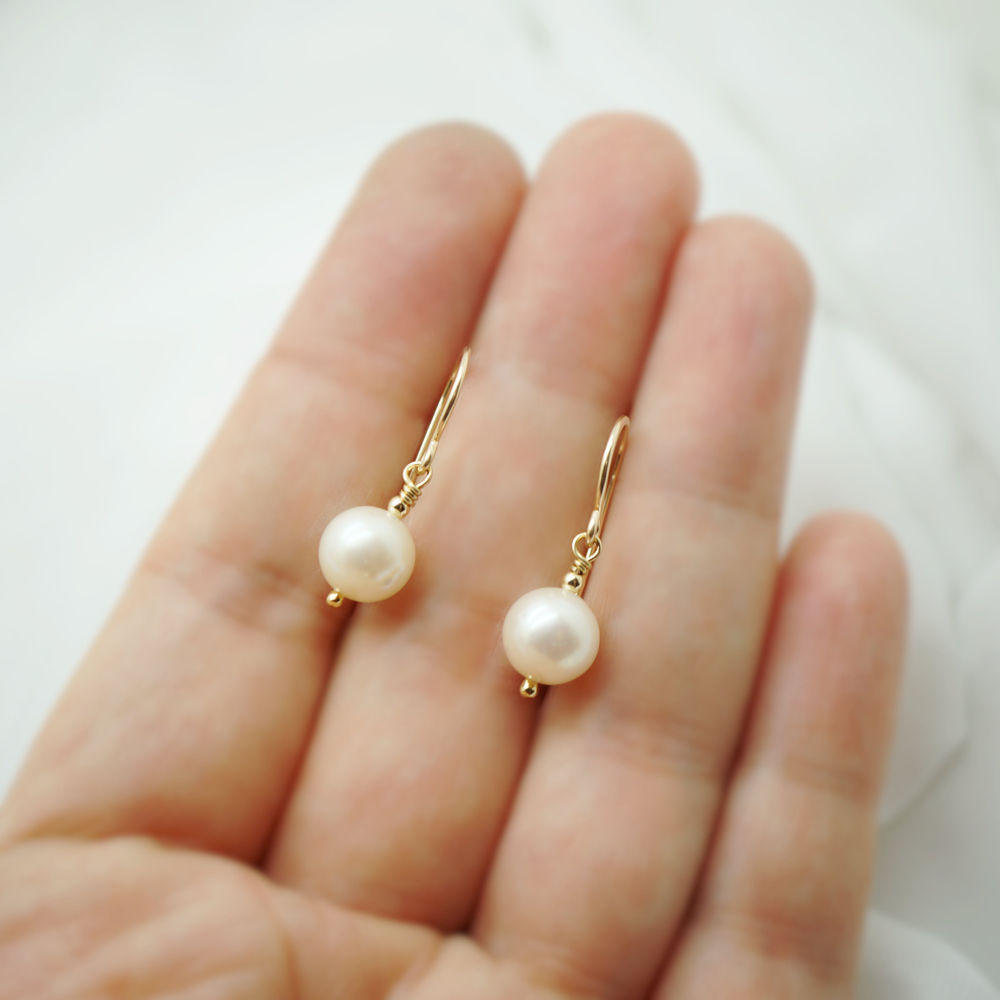 Handgemaakte 14k gold filled oorbellen met zoetwaterparels gepresenteerd op een hand, grootte en glans duidelijk zichtbaar.
