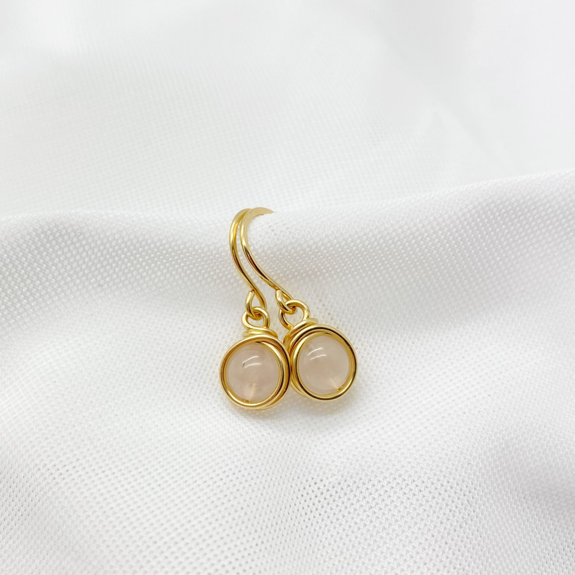 Gouden oorbellen met rozenkwarts liggend op wit oppervlak, minimalistisch en chic.