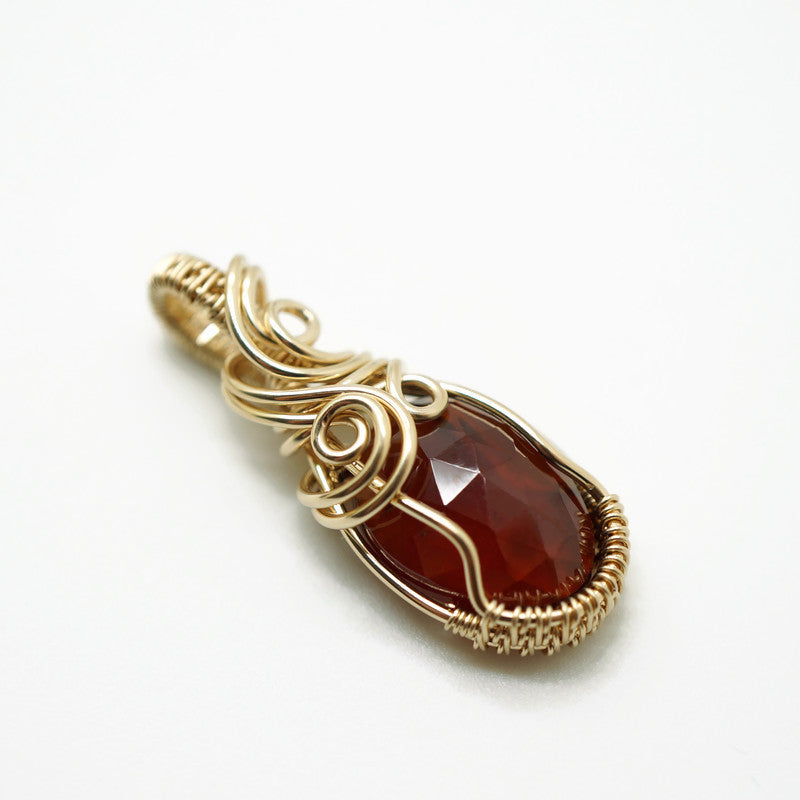 Zijaanzicht van de hanger met spessartien granaat, met zicht op de wire wrap techniek.