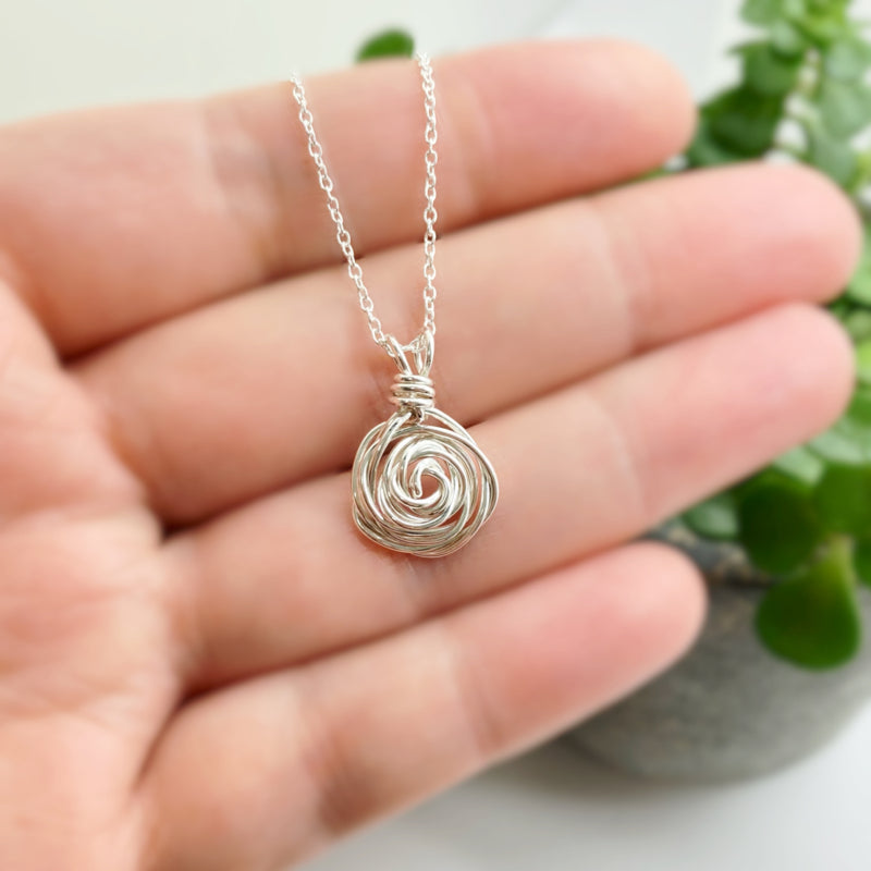 Close-up van de handgemaakte roos hanger aan een fijne zilveren ketting.
