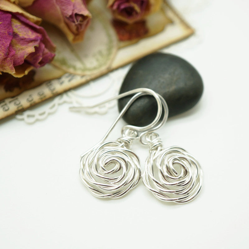 Close-up van handgemaakte zilveren oorbellen in roosvorm, gemaakt met wire wrap techniek.