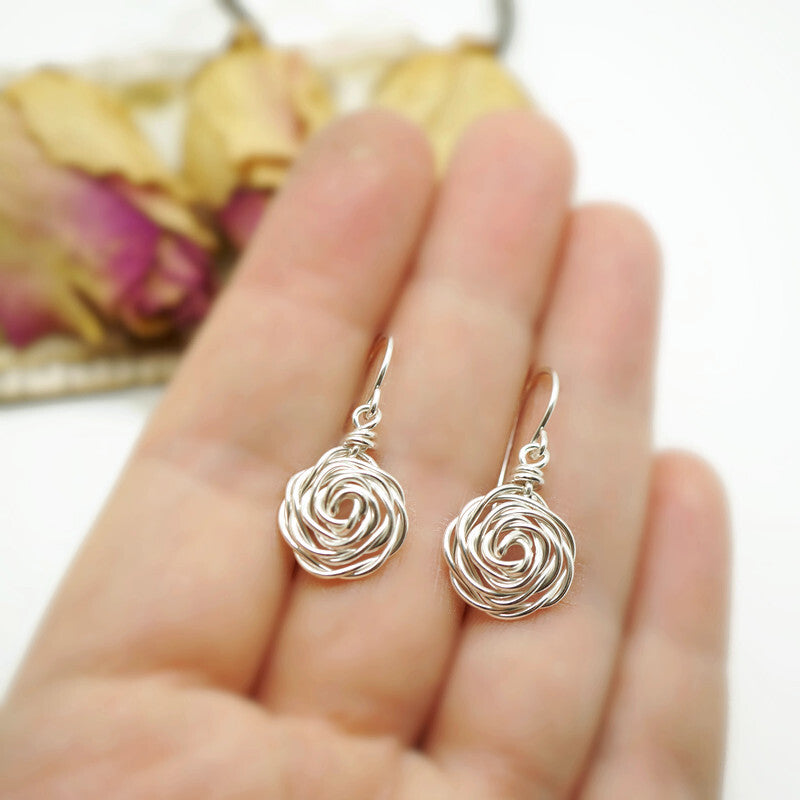 Kleine zilveren wire wrap roos oorbellen getoond in een hand voor schaalweergave.