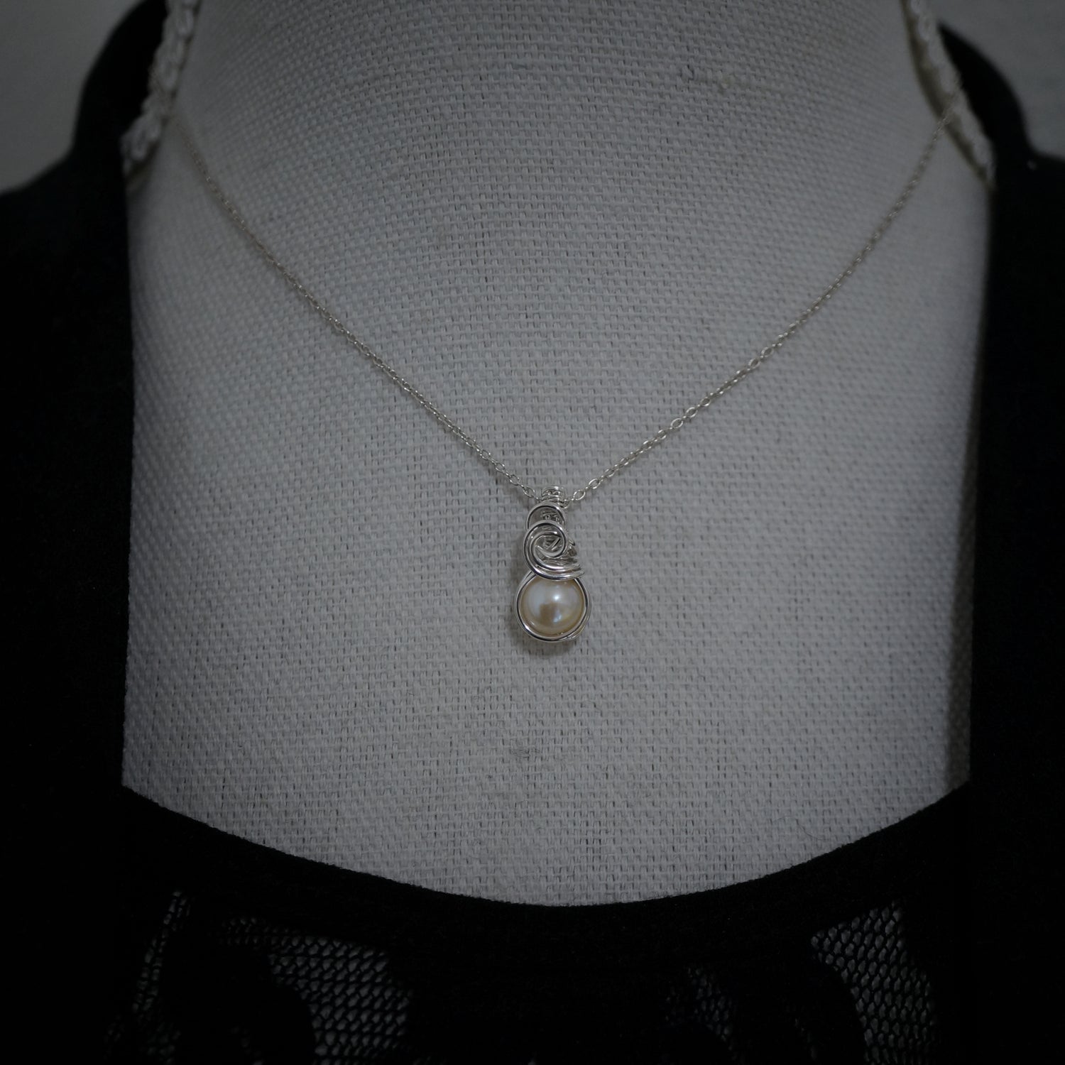 Zilveren wire wrap hanger met parel gedragen aan collier, minimalistische stijl