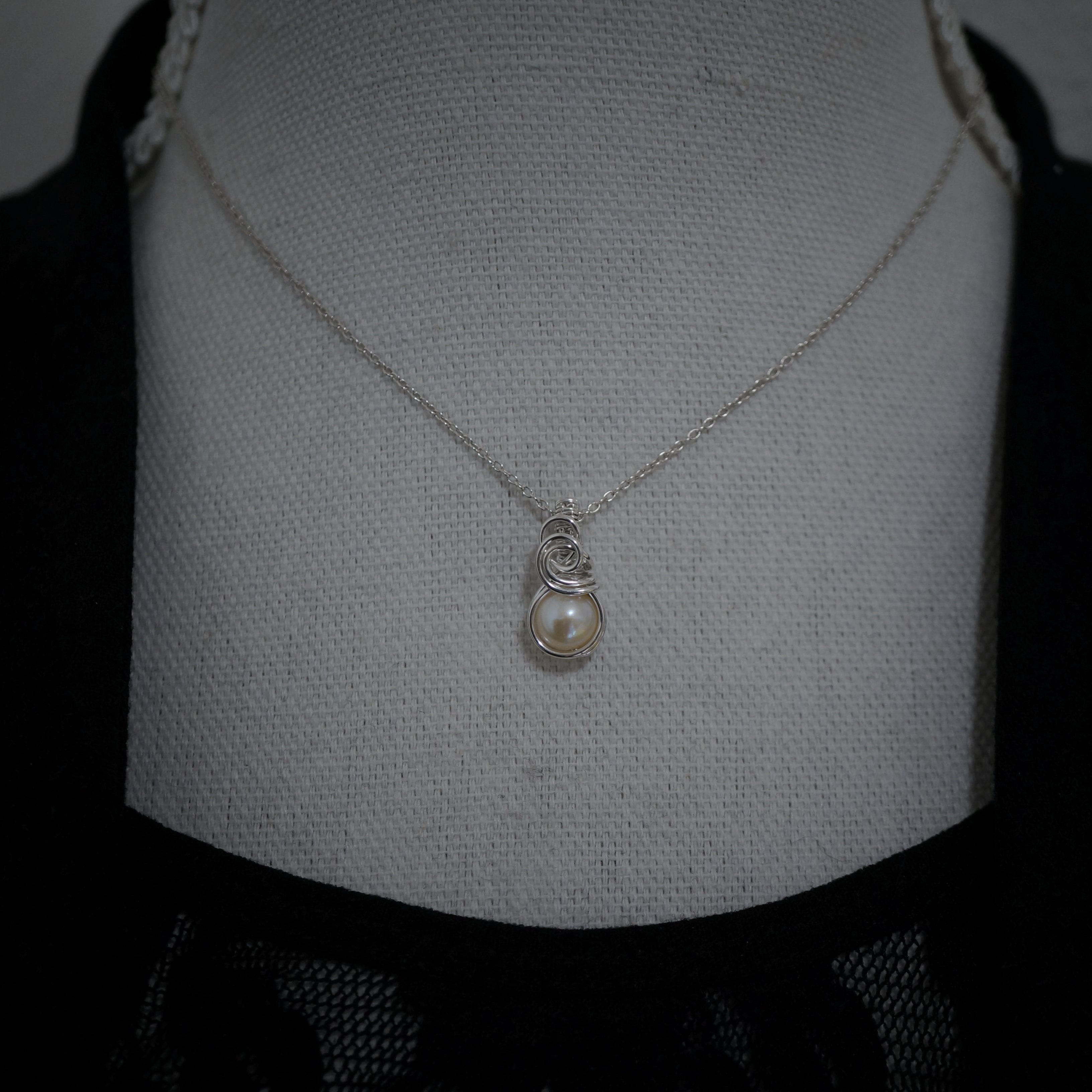 Zilveren wire wrap hanger met parel gedragen aan collier, minimalistische stijl