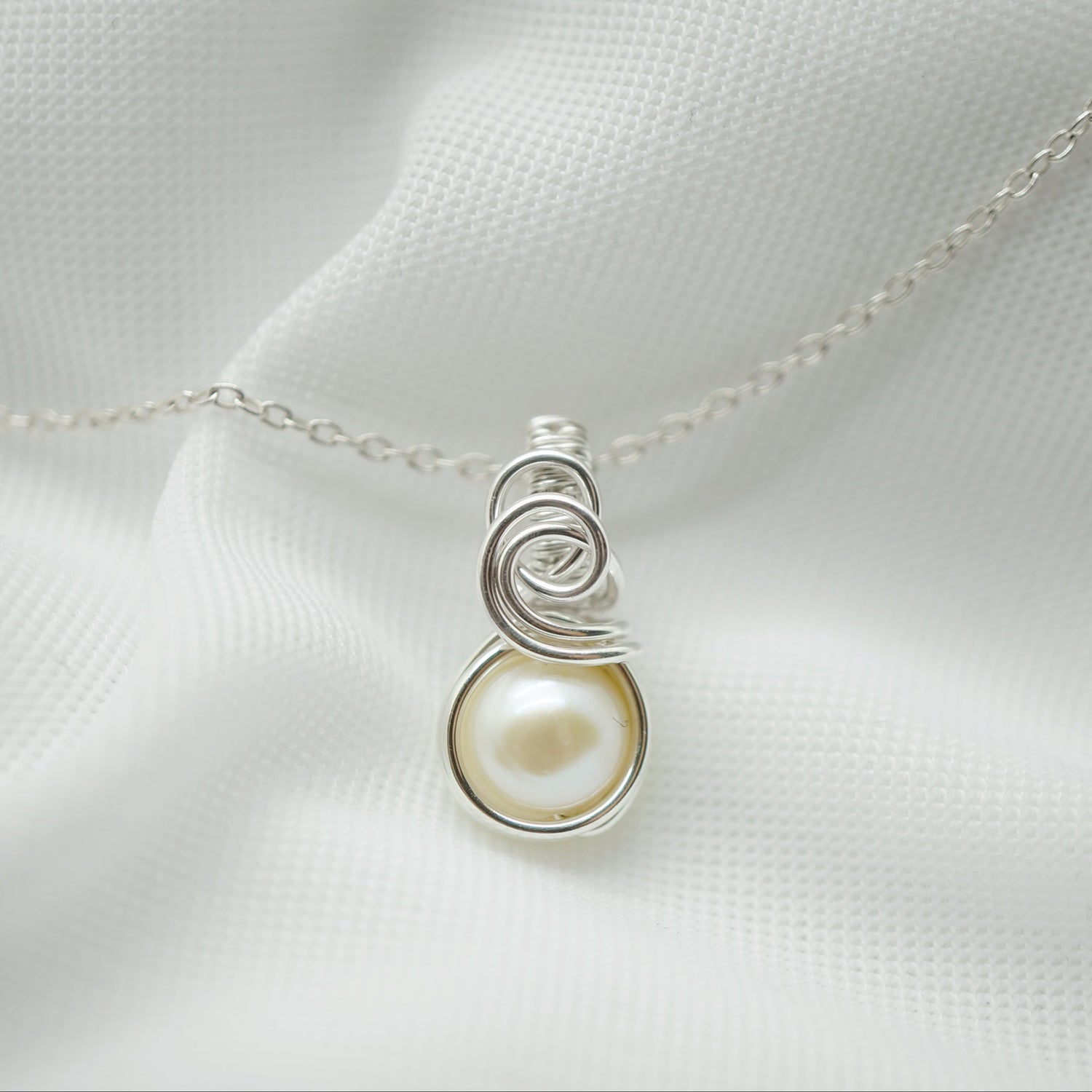 Close-up: Sterling zilveren wire wrap hanger met creme zoetwaterparel handgemaakt detail
