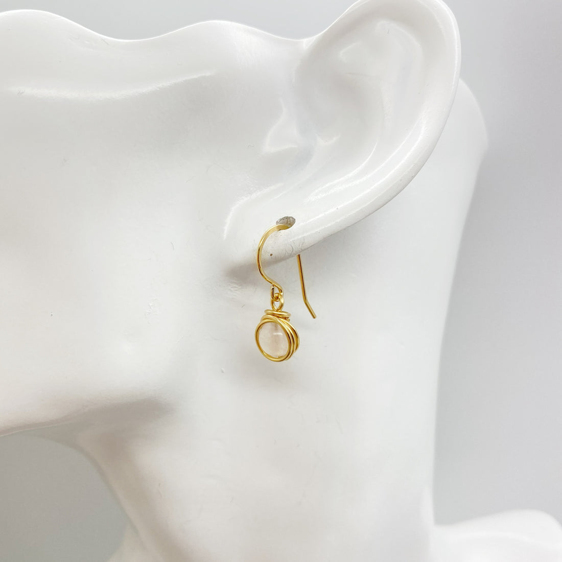 Zijaanzicht van de oorbel met lichtroze rozenkwarts en handgewikkelde gold filled draad.