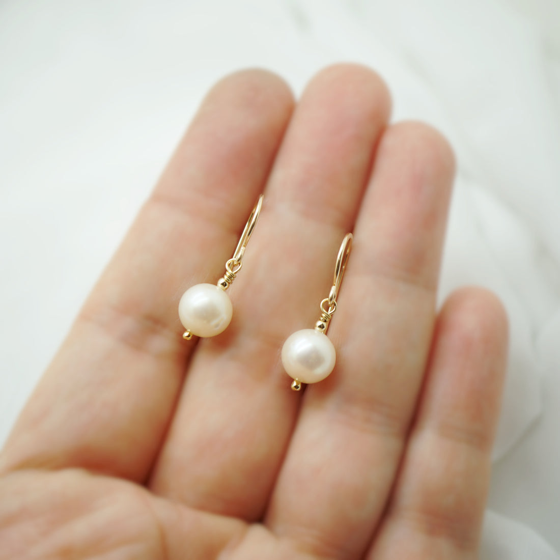 Handgemaakte 14k gold filled oorbellen met zoetwaterparels gepresenteerd op een hand, grootte en glans duidelijk zichtbaar.